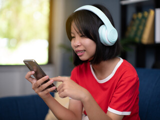 Smiling pretty girl wearing headphones using smartphone, interested child listening to favorite music, chatting in social network or playing game online.