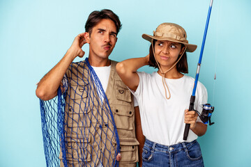 Young mixed race fisher couple isolated on blue background touching back of head, thinking and...