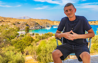 Traveler tourist on chair Lindos Beach bay panorama Rhodes Greece.