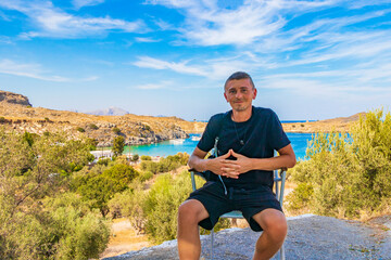 Naklejka na ściany i meble Traveler tourist on chair Lindos Beach bay panorama Rhodes Greece.