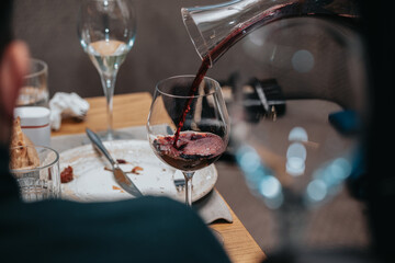 Elegant waiter pours red wine from bottle into glass at restaurant. Sommelier tasting wine in restaurant. Copy space for text menu elegant or recipe on dark background.