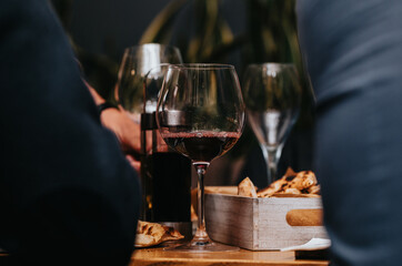 Elegant waiter pours red wine from bottle into glass at restaurant. Sommelier tasting wine in restaurant. Copy space for text menu elegant or recipe on dark background.