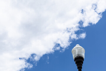 Exterior light post with glass fixture isolated against a blue sky with white clouds, creative copy space, horizontal aspect
