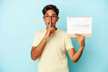 Young mixed race man holding calendar isolated on blue background keeping a secret or asking for silence.