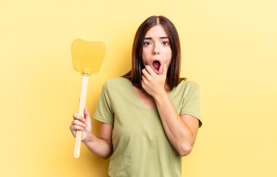 Young Hispanic Woman With Mouth And Eyes Wide Open And Hand On Chin. Kill Flies Concept