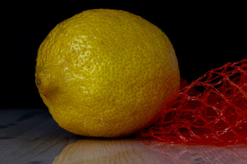 whole lemon with a red mesh to strengthen immunity, lying on a wooden table, on a black background