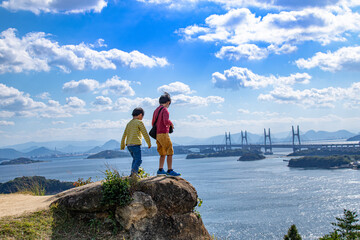 瀬戸大橋・瀬戸内海を眺める兄弟　岡山県倉敷市　Asian boys standing on the rock and watching the view of Setonaikai, Inland Sea of Japan, and Seto Ohashi bridge in Kurashiki city, Okayama pref. Japan.