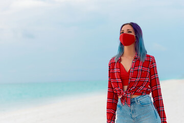 Happy young woman wearing face protective mask on the beach near the sea. Travel concept