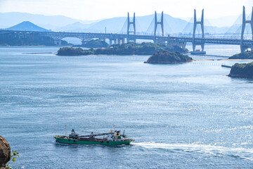Obraz premium 瀬戸大橋と船の風景 岡山県倉敷市 The view of Seto Ohashi bridge at Setonaikai, Inland Sea of Japan, and a freight vessel in Kurashiki city, Okayama pref. Japan
