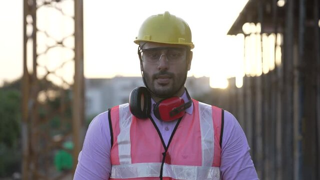 Portrait of Indian male civil engineer,worker on construction site. successful Asian male industrial worker looking at camera wearing high vest and hard hat helmet with crossing his hands.