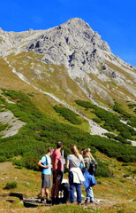 Fototapeta na wymiar 4 junge Wanderer vor dem Aufstieg zum Saulakopf im Vorarlberg mit steilem Fels und grünen Wiesen