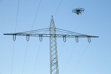 Drohne mit Kamera an Bord, die in einen Himmel fliegt, Strommast, Kabel und Isolatoren im...