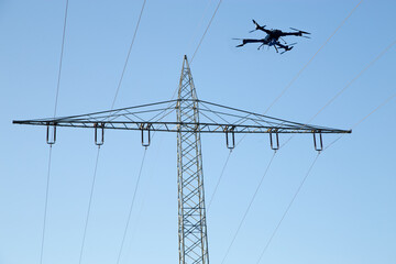Drohne mit Kamera an Bord, die in einen Himmel fliegt, Strommast, Kabel und Isolatoren im Hintergrund - obrazy, fototapety, plakaty