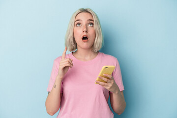 Young caucasian woman holding mobile phone isolated on blue background pointing upside with opened mouth.