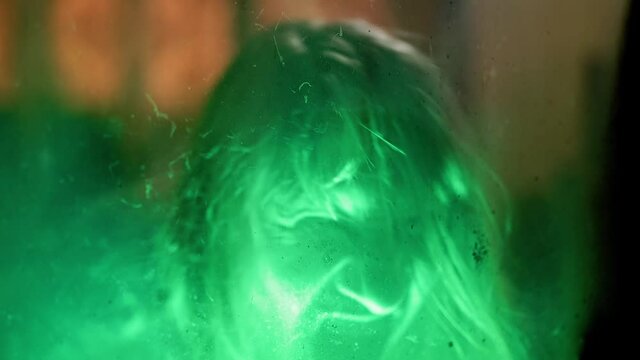 Scary ghost woman screaming through dirty glass on dark background. Monster devil or female spirit dead characters.