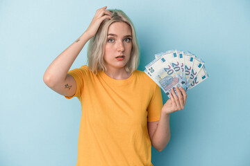 Young caucasian woman holding bills isolated on blue background being shocked, she has remembered important meeting.