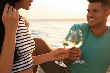 Lovely couple having picnic near river at sunset, focus on glasses