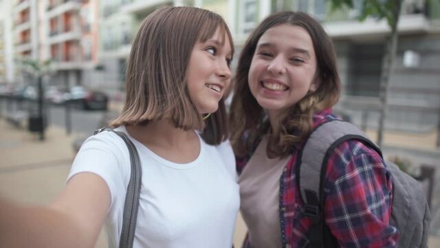 Joyful teenage bloggers showing thumbs up smiling talking looking at camera. Selfie POV of confident charming positive Caucasian girls blogging standing on city street outdoors