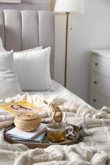 Stylish tray with different interior elements and tea on bed indoors
