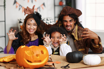 Happy african american family parents and little boy son in Halloween costumes making jack o lantern