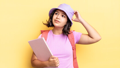 young hispanic woman feeling puzzled and confused, scratching head. back to school concept