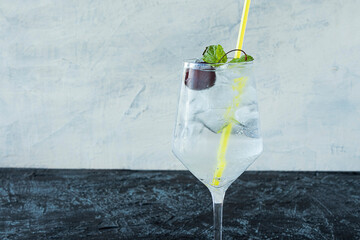 cold drink in a glass with a yellow drinking straw on a black and white background. a refreshing cocktail on a summer day with ice, cherries and mint.