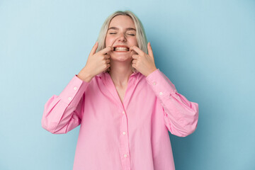 Young caucasian woman isolated on blue background smiles, pointing fingers at mouth.