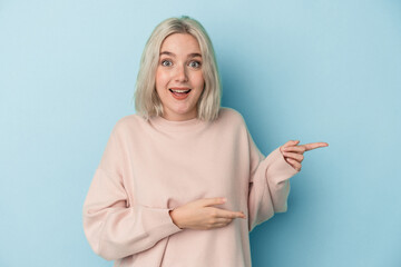 Young caucasian woman isolated on blue background excited pointing with forefingers away.