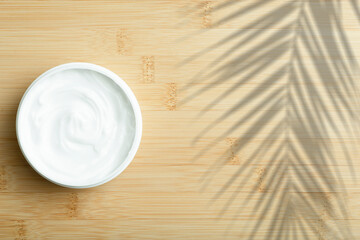 Cosmetic cream background. White cosmetic cream for skin and body in an open white jar on a wooden bamboo empty background.