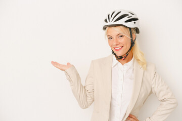 Young business Russian woman holding bike helmet isolated on white background showing a copy space on a palm and holding another hand on waist.