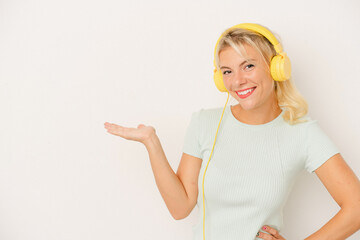 Young Russian woman listening to music isolated on white background showing a copy space on a palm and holding another hand on waist.