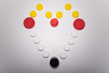 Tapones de botellas de plástico, de diferentes tamaños y colores, formando un corazón sobre un fondo blanco.