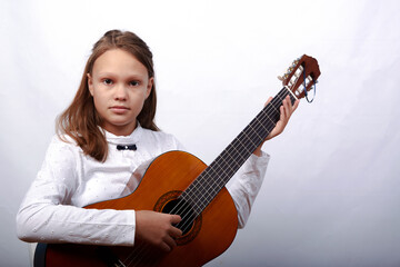 Fototapeta premium an 11-year-old girl is practicing a melody on a guitar on a blue background