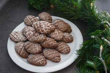 Chocolate cookies on a white plate. Christmas biscuits close up photo. Fir tree branches, anise stars, cinnamon sticks pine cone shaped cookies. Sweet food top view photo. 