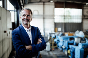 Male business professional with arms crossed standing at metal industry