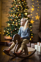 Fototapeta na wymiar little girl rides a wooden horse at christmas under the tree