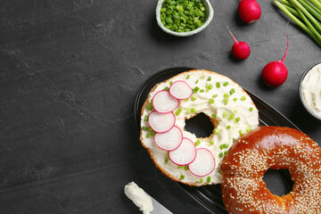 Delicious bagel with cream cheese, green onion and radish on black table, flat lay. Space for text