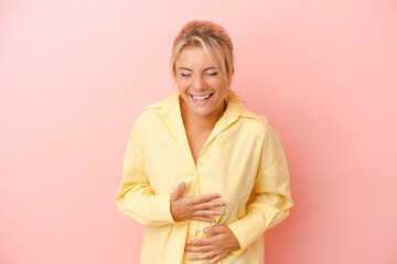 Young Russian woman isolated on pink background laughs happily and has fun keeping hands on stomach.
