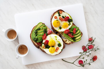 breakfast of fried egg sandwich with avocado, tomatoes and basil pesto on the table and coffee