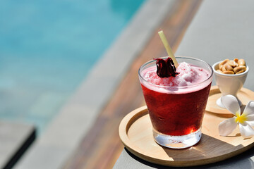 Glass of cold roselle juice on border of a swimming pool