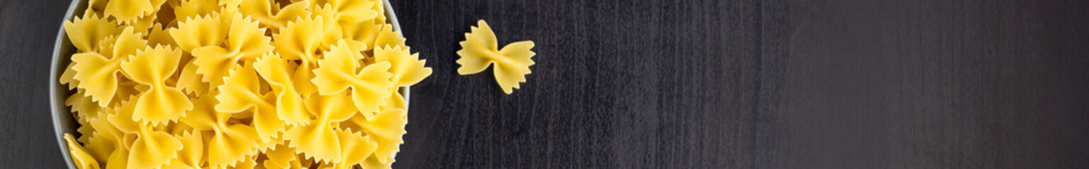 banner of Top view of black background with italian raw farfalle or pasta in bowl with copy space