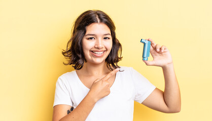 young hispanic woman smiling cheerfully, feeling happy and pointing to the side. asthma concept