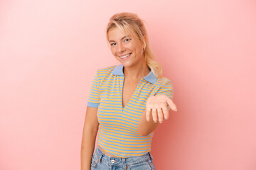 Young Russian woman isolated on pink background stretching hand at camera in greeting gesture.