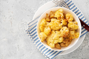Baked cauliflower in a white bowl on a gray background. Homemade baked cauliflower with butter, cream and garlic. Tasty vegetarian food.