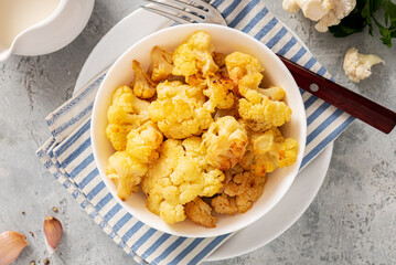 Baked cauliflower in a white bowl on a gray background. Homemade baked cauliflower with butter, cream and garlic. Tasty vegetarian food.