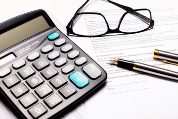 On the desktop are a black calculator, a fountain pen, and black-framed glasses. Workplace close-up. Business concept