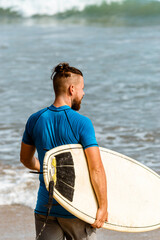 Surfer z deską na wybrzeżu przygotowujący się do pływania. - obrazy, fototapety, plakaty