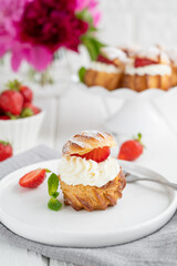Delicious homemade small cakes profiterole choux pastry with custard, strawberry and icing powder on the white wooden background. Copy space.