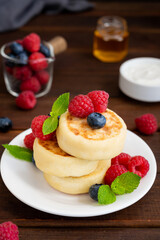 Cottage cheese pancakes with fresh berries, sour cream and honey on a dark wooden background. Homemade traditional Ukrainian and Russian syrniki.