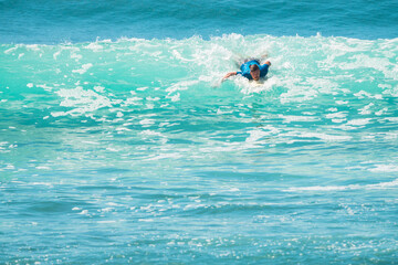 Surfer mężczyzna łapiący falę na desce na tle niebieskiego oceanu i błękitnego nieba. © insomniafoto